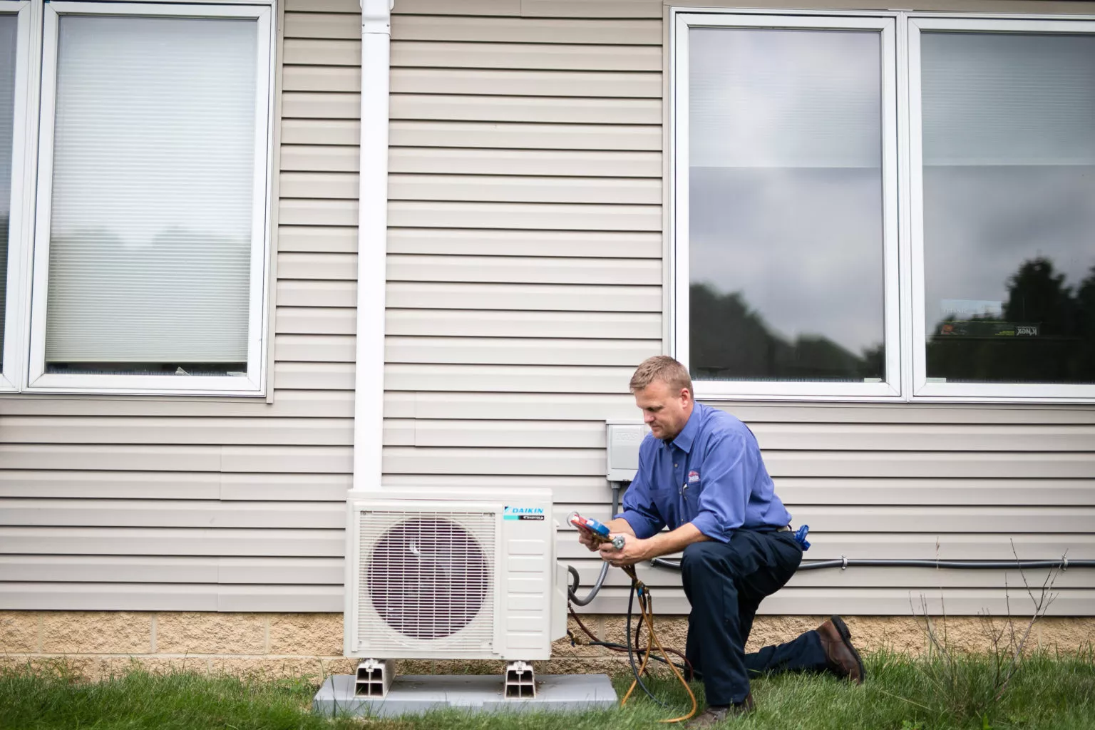 Technician repairing outdoor AC unit beside a home with beige vinyl siding.