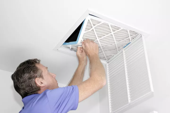  Man in a light purple shirt removing a dirty air filter from the ceiling vent 
